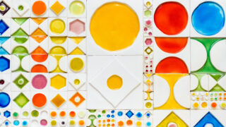 A close-up of a ceramic work that consists of different sized, white quadrilateral pieces with colorful forms in them.